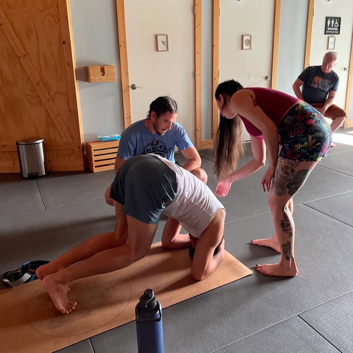 Teachers giving hands-on assists around the room during a class at Renegade Yoga Institute