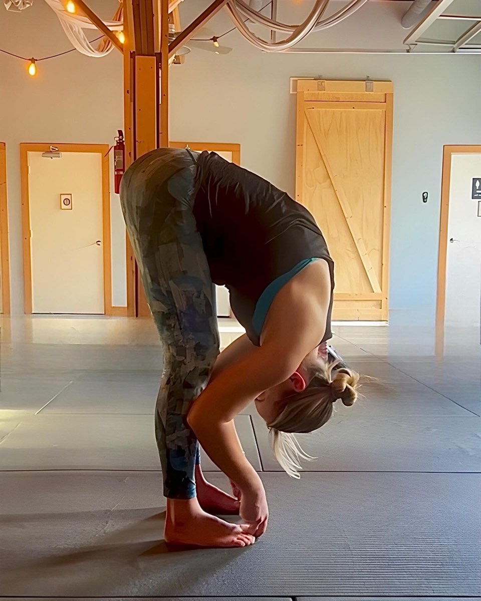 A student in a standing forward fold in the morning light at Renegade Yoga