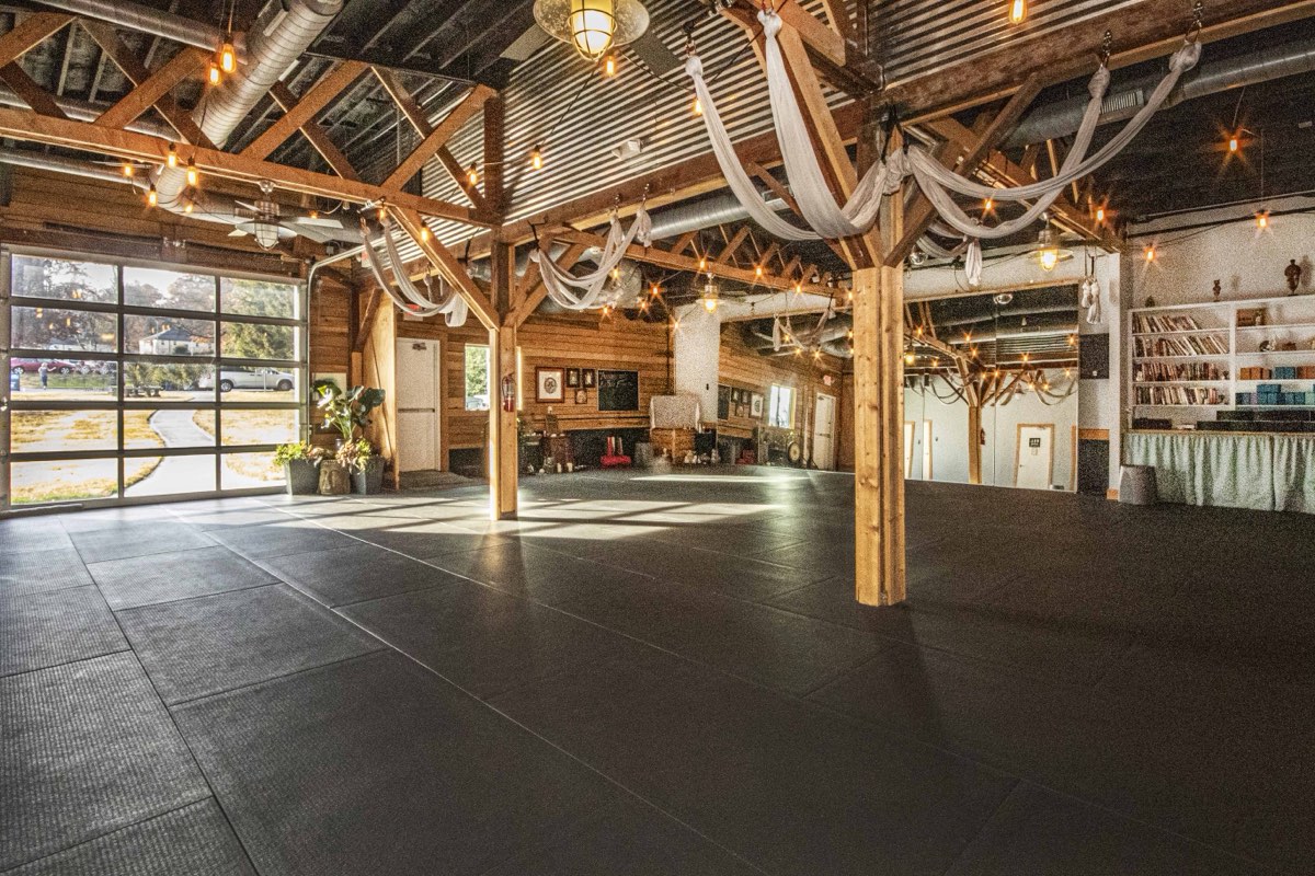 The main practice room at Renegade Yoga: padded floor, timber trusses, aerial hammocks and an open garage door